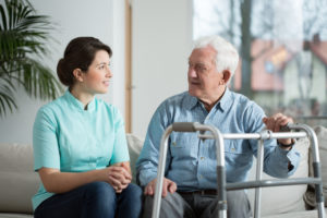 A woman sits beside an elderly man with a mobility frame